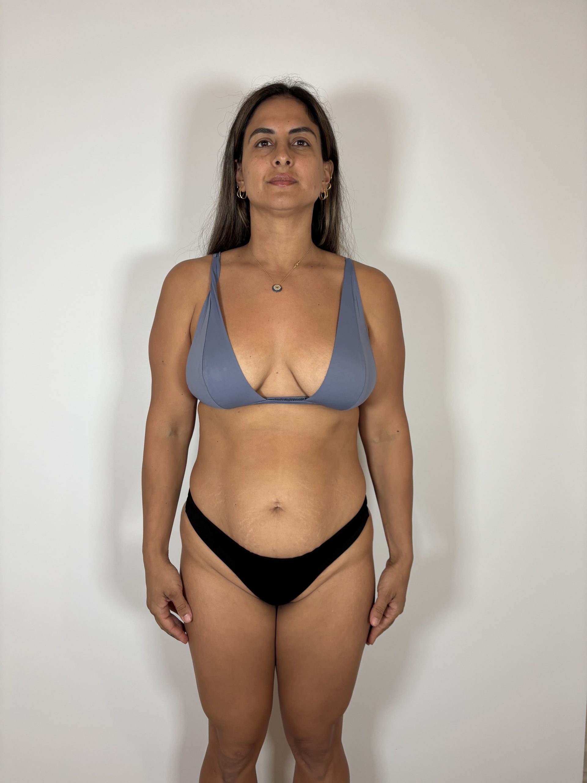 A woman stands facing forward against a plain white background, wearing a gray bikini top and black bikini bottoms.
