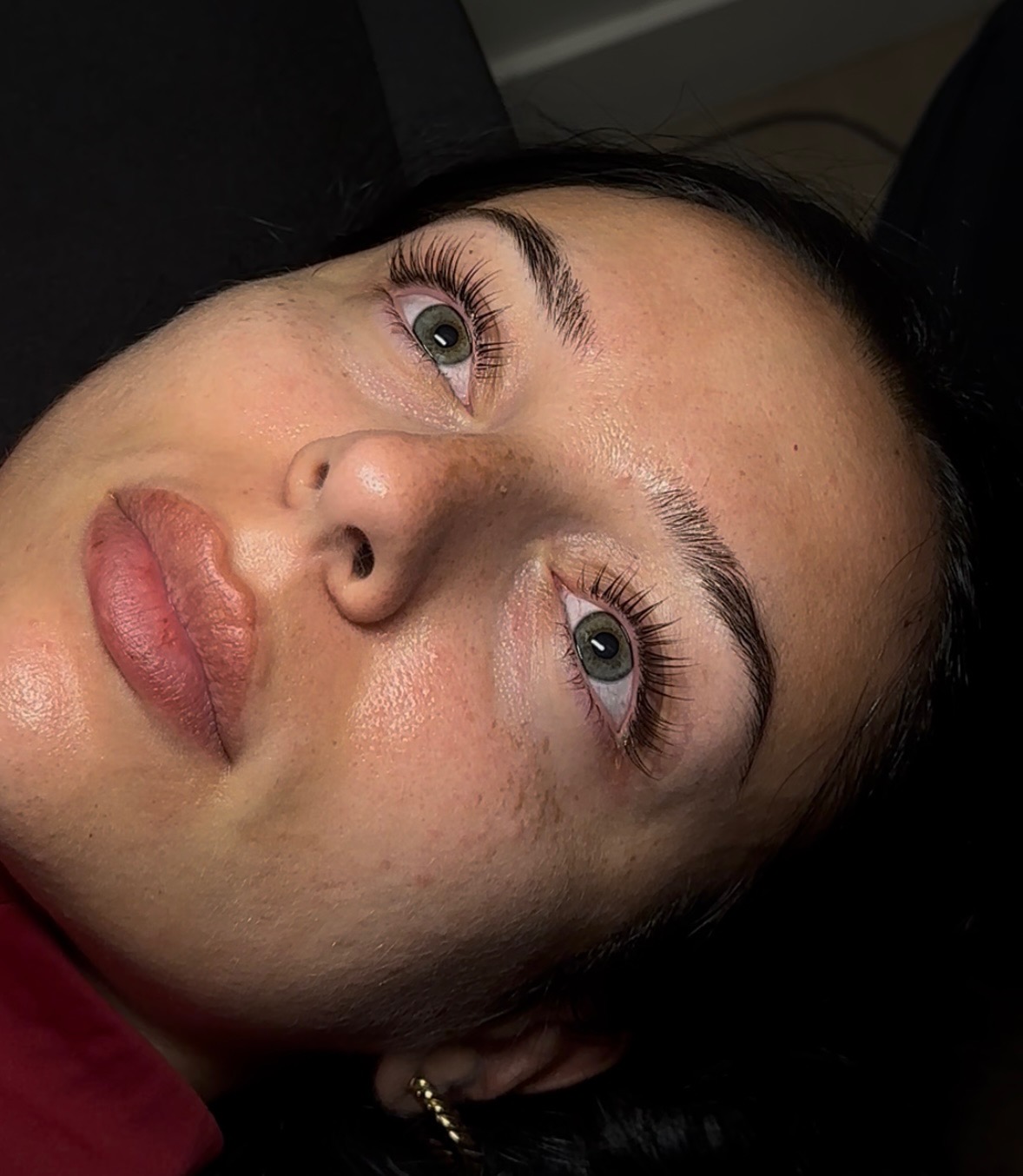 A person with green eyes, full lips, and clear skin lies back, looking upward under soft lighting.