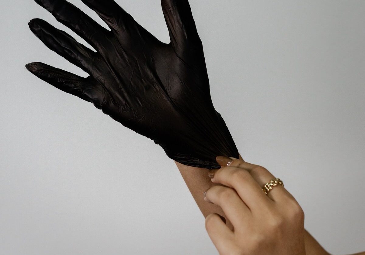 A person puts on a black disposable glove against a plain light background.